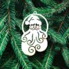 Boule Pere Noel Un ornement en bois en forme de Père Noël avec une barbe tourbillonnante est suspendu aux branches vertes du sapin.