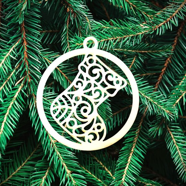 Boule botte Un ornement circulaire décoratif représentant un bas complexe est suspendu à des branches de pin vertes.
