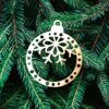 Boule perforée flocon haut Un ornement de Noël en bois avec un nœud et un flocon de neige est suspendu aux branches vertes d'un sapin.