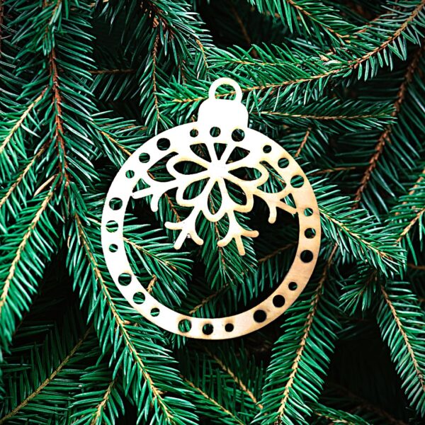 Boule perforée flocon haut Un ornement de Noël en bois avec un nœud et un flocon de neige est suspendu aux branches vertes d'un sapin.