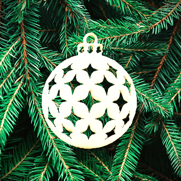 Boule pleine perforee etoiles Un ornement décoratif en bois découpé au laser en forme de boule de Noël est suspendu aux branches d'un pin vert.