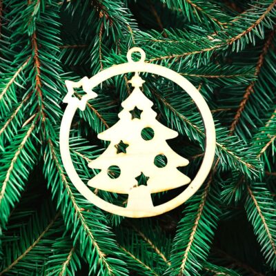 Un ornement de sapin de Noël en bois avec des découpes en forme d'étoiles est suspendu à des branches de pin vertes.