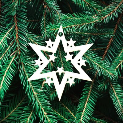 Un ornement blanc en forme d'étoile avec des étoiles découpées est suspendu aux branches vertes d'un pin.